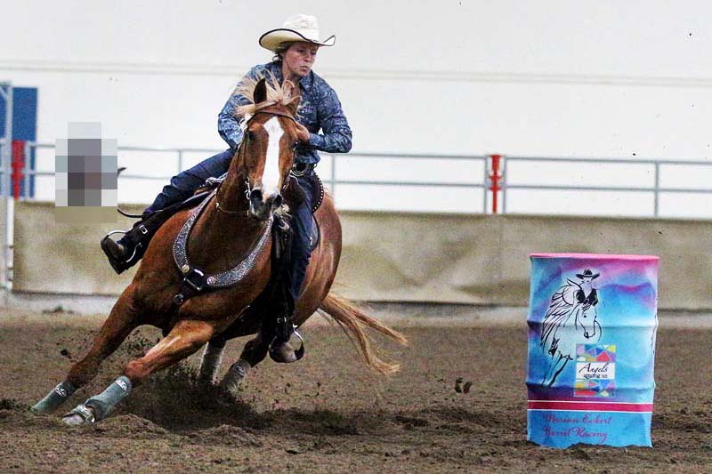The rider in barrel racing circles around a blue barrel.