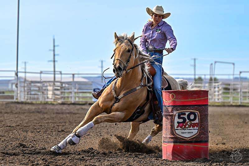 The rodeo rider circles around a red barrel.