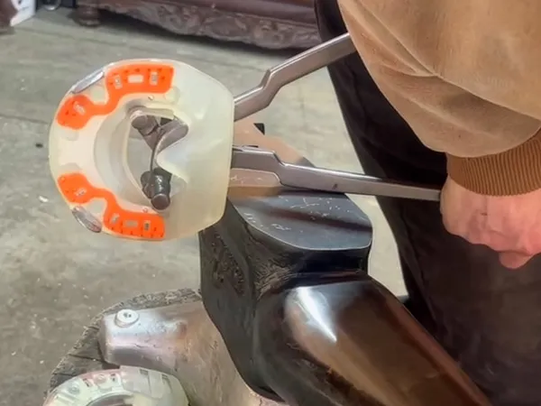 A farrier is widening a composite horseshoe with a metal core using a modified shoe spreader.
