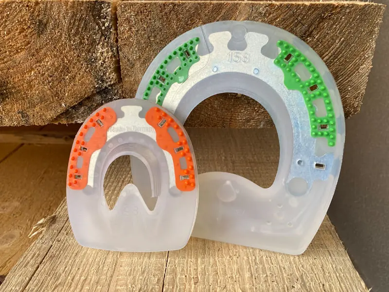 Two composite horseshoes without quarter clips in different sizes for small and large hooves, with green and orange inserts