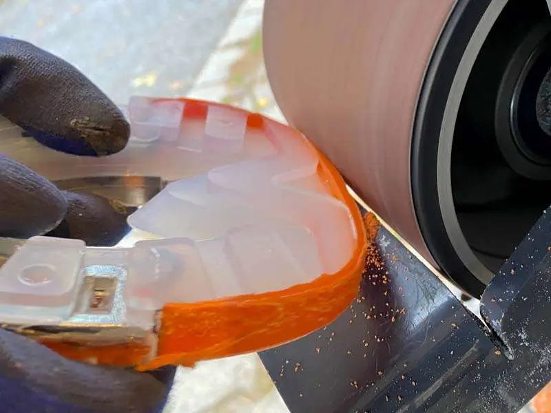 Horseshoe with plastic coating, welded with an orange strip, is adjusted to the hoof using a belt grinder