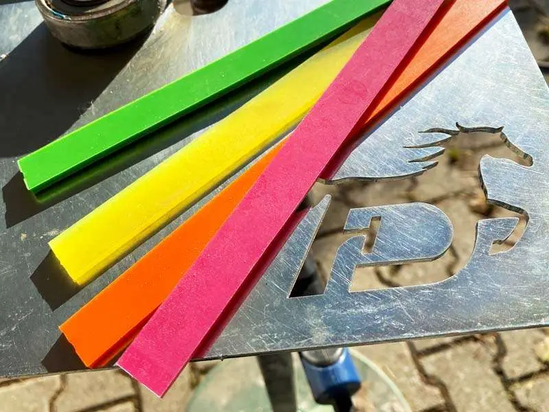 Color strips in green, yellow, pink and green for horseshoes with plastic coating are on a metal plate