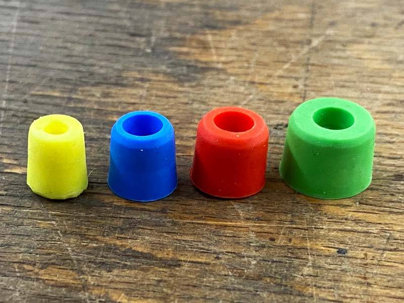 plastic closure plugs in various colors, used for sealing the threaded holes in horseshoes, are arranged side by side on a wooden floor