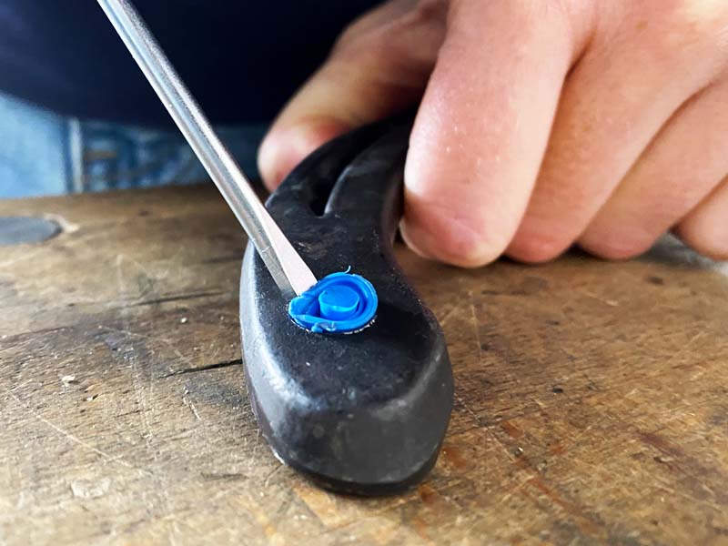 a hand holds a steel shoe, while a slotted screwdriver is used to remove a blue closing plugfrom a stud hole