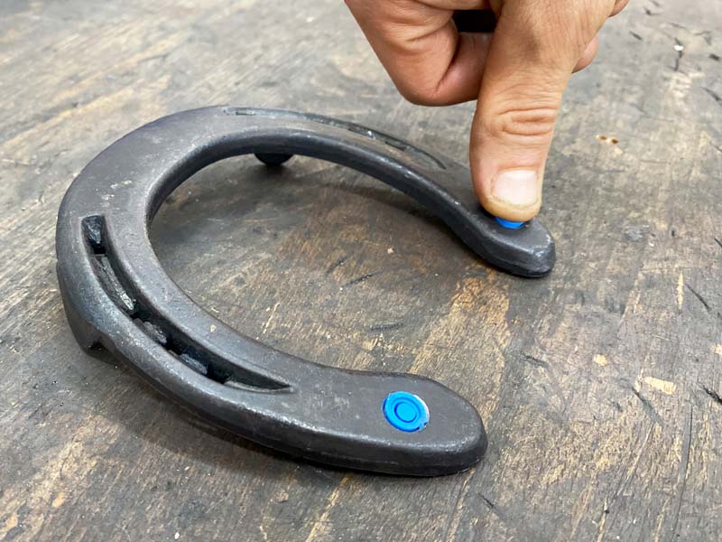 someone is pressing a blue closure plug into the threaded hole of a steel horseshoe using their thumb