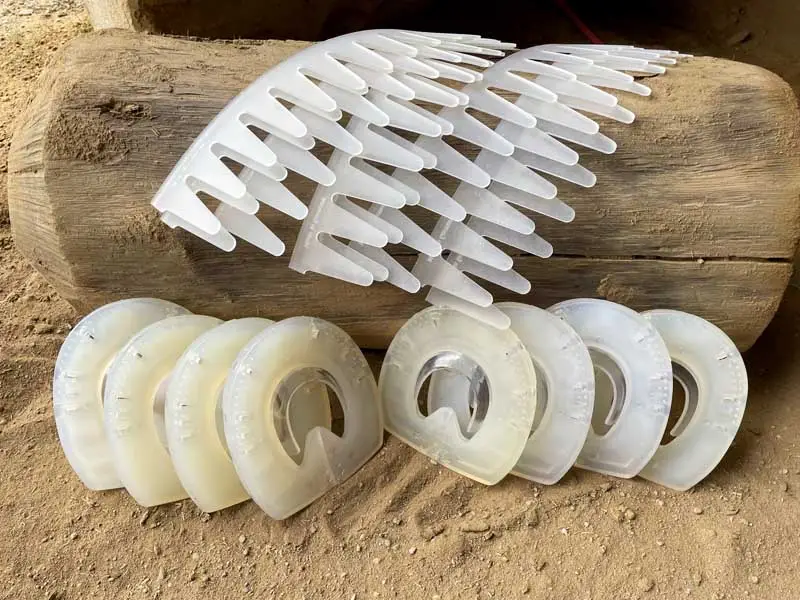 Eight dummy horse shoes are placed in the sand in front of a tree trunk, with eight adhesive collars placed on them.