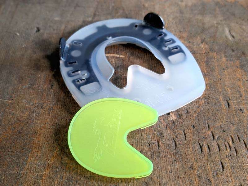 A composite horseshoe with a closed sole area and a matching yellow sole protector to close the opening in the horseshoe lie on a wooden floor.