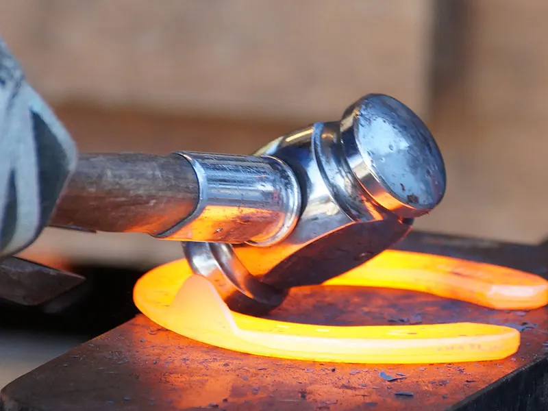 The farrier shapes the glowing hot horseshoe with the forging hammer.