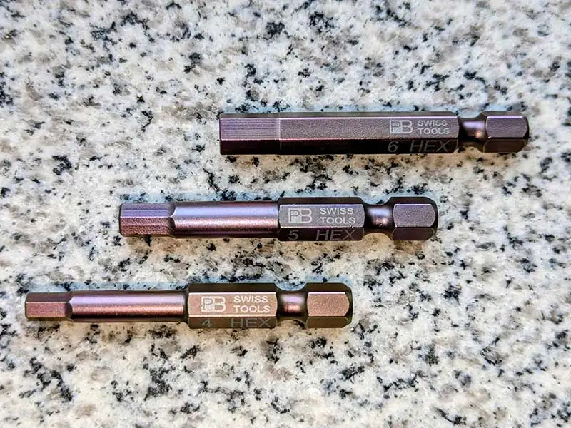 Three different sizes of the PrecisionBit from Swiss Tools in the E 6.3 1/4 inch shape lying on a stone surface.