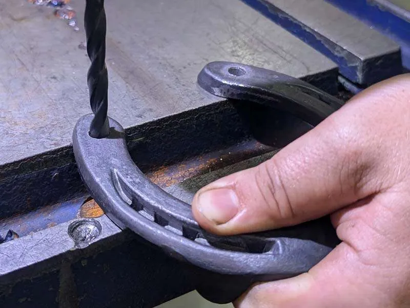 Le maréchal-ferrant perce un trou dans un fer à cheval à l'aide d'une mèche en acier pour y enfoncer un crampon à souder.