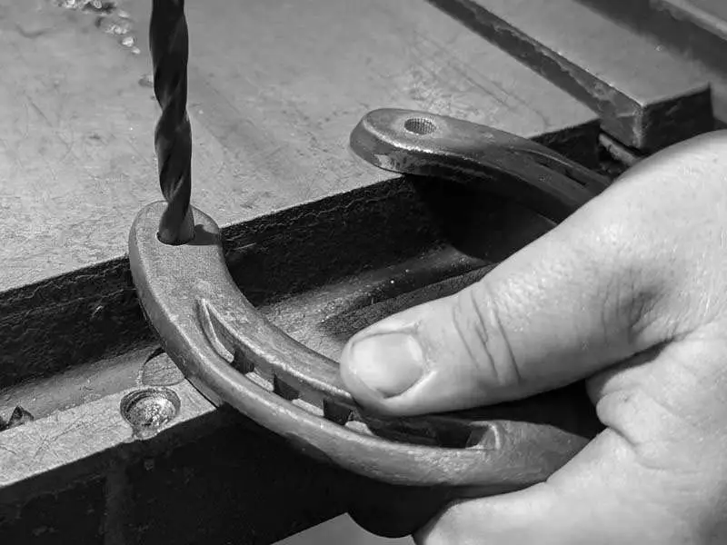 A hole is being drilled into a steel shoe using a metal drill bit to insert the stud afterwards.