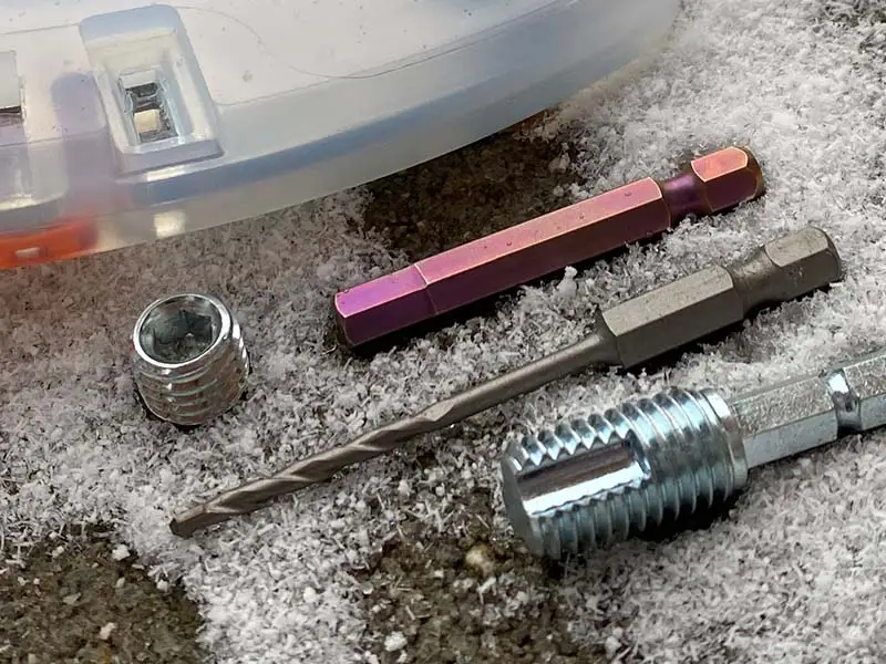 The stud change tools for the alternative horseshoe lying in the snow — a hex socket set screw, a hex bit insert, a thread cleaner, and the Projahn masonry drill bit.