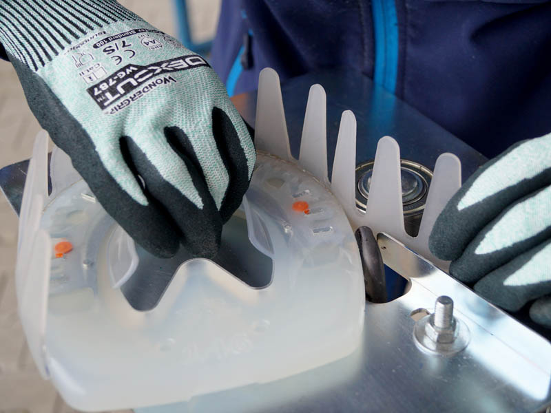 farrier hands wearing cut-resistant gloves are holding a plastic horseshoe and a green strip while welding both pieces with the help of a special device.