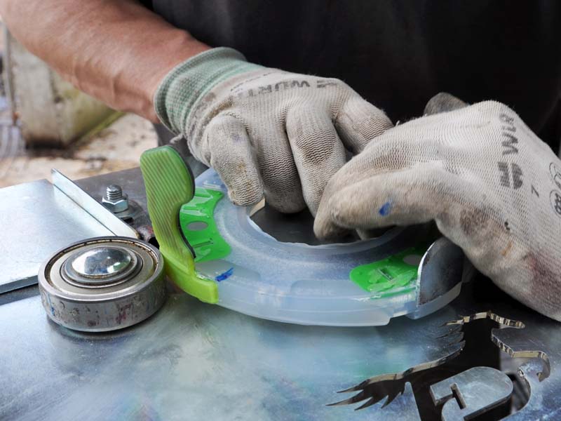 farrier hands wearing work gloves are rolling a clipped horseshoe around the ball bearing of a special fixture to plastic weld the glue-on tab to the horseshoe