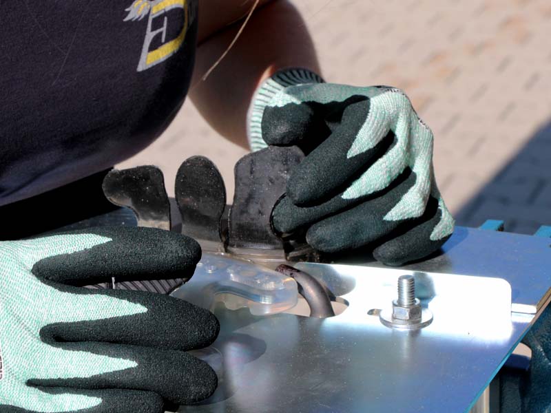 a farrier is plastic welding an open-toed shoe with an adhesive tab, she is wearing gloves and uses a plastic welding device