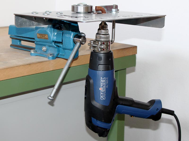 a Steinel hot air gun is connected to a welding device designed for the plastic welding of adhesive horseshoes, and this assembly is secured in a light blue vise