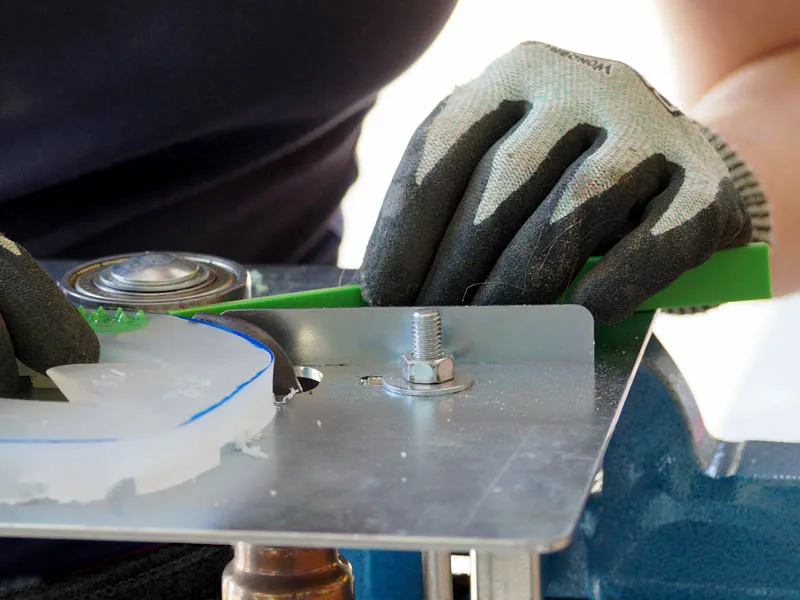manos con guantes de protección anticorte sostienen un herraje de plástico y una banda de color verde mientras se sueldan utilizando un dispositivo especial